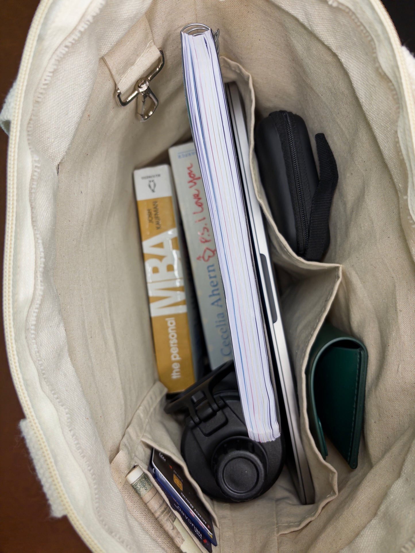 Open beige bag with items including a notebook, wallet, and phone.
