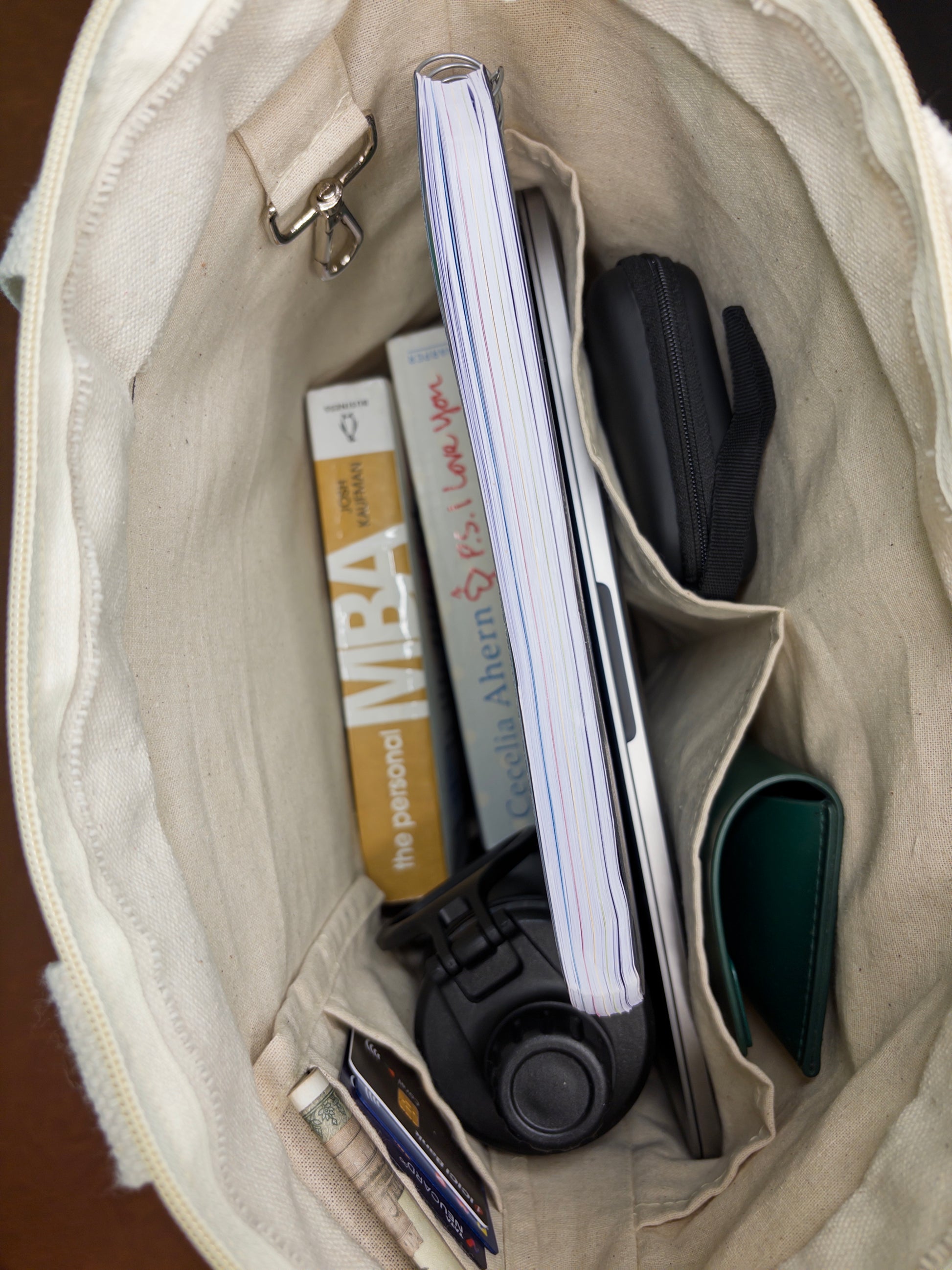 Open beige bag with items including a notebook, wallet, and phone.