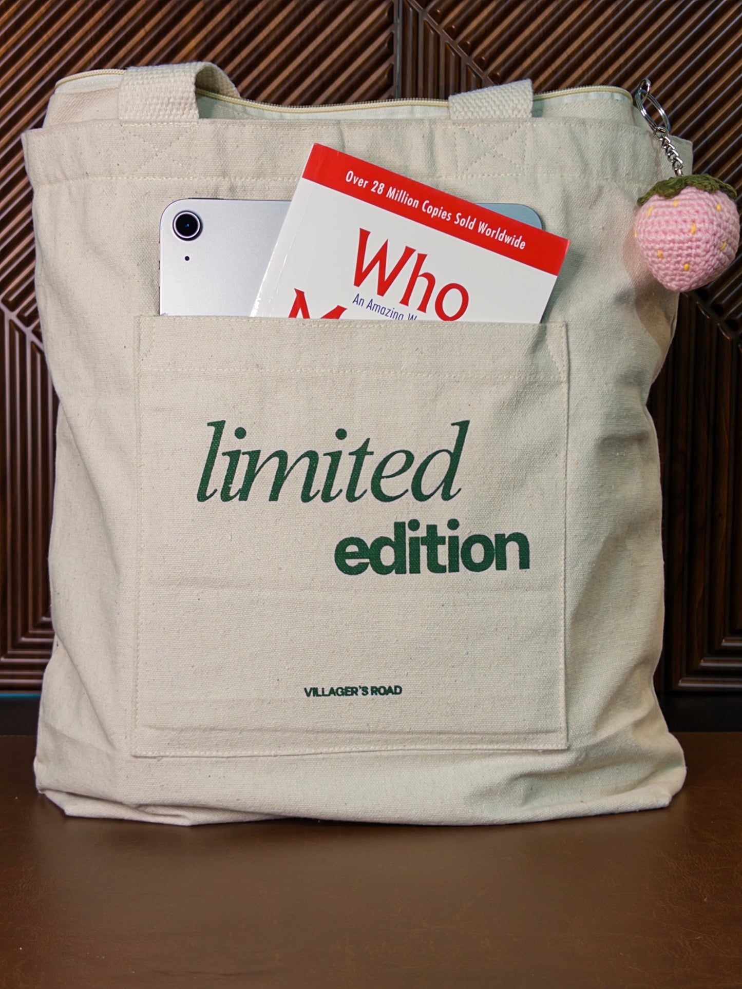 Beige tote bag with 'limited edition' text, phone, and book inside, on a wooden surface.